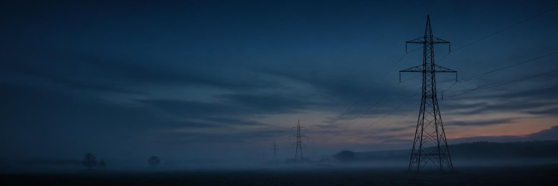 Hochspannungsleitungen über nebliger Landschaft in der Dämmerung
